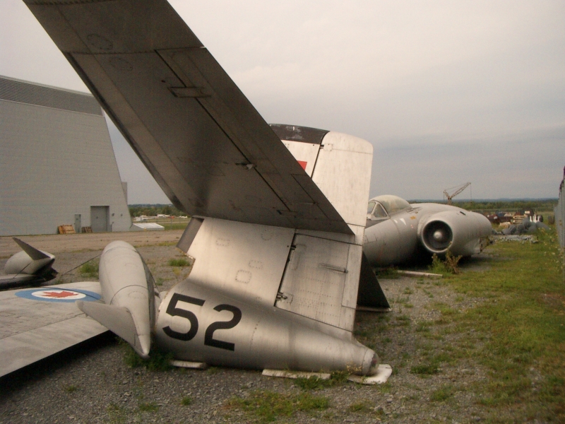 CF-100 jet fighter from the fifties in pieces in a field adjacent to National Aviation Museum awaits restoration. Picture taken through chain- link fence.